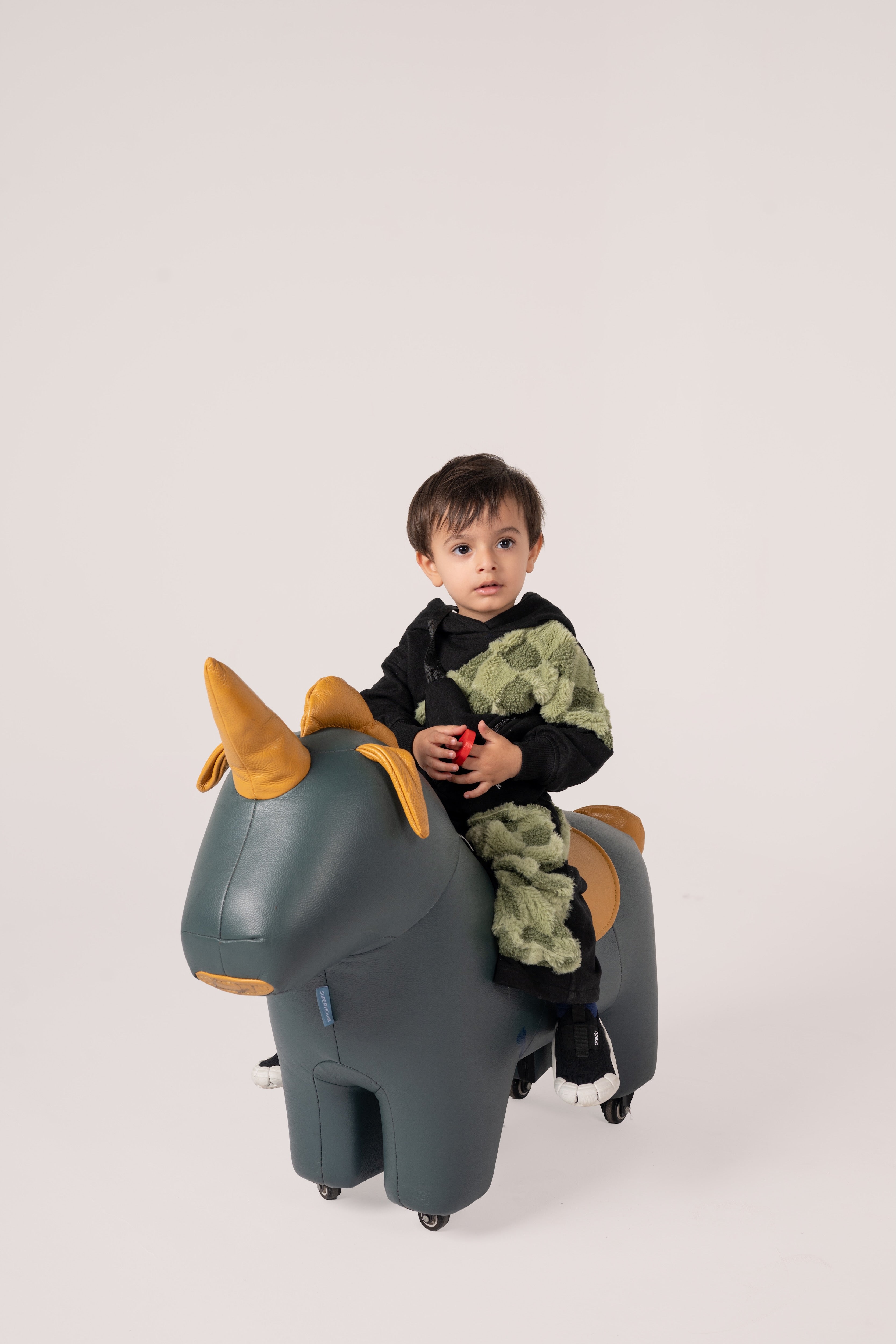 Young child sitting on a luxurious dark green leather unicorn ride-on toy with golden horns and wheels