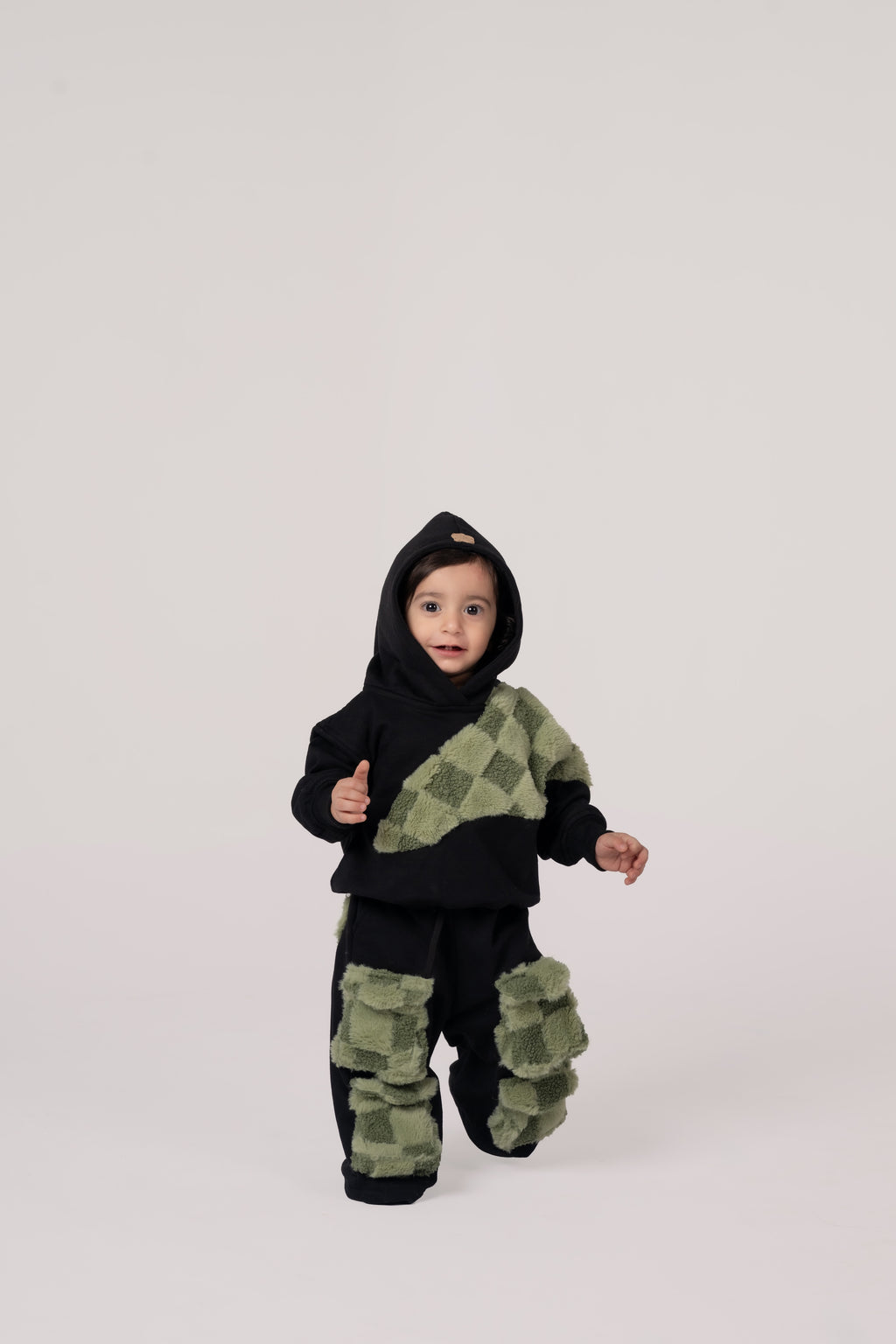 Toddler in luxurious black hoodie and pants with green textured checkered accents on minimalist background