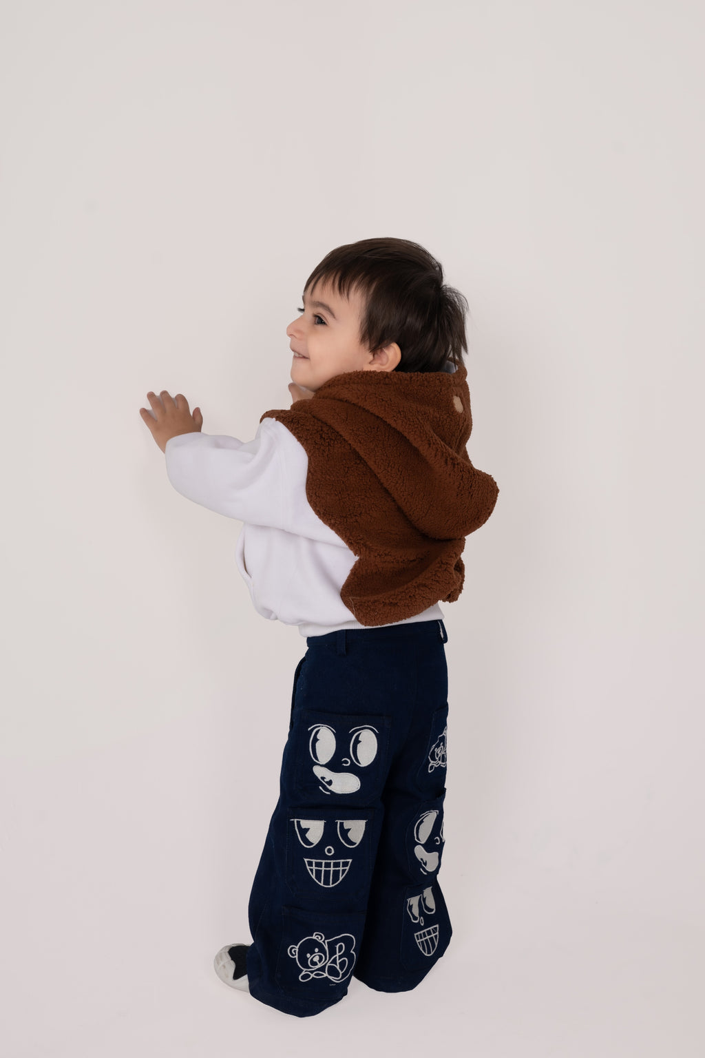 Stylish toddler in brown furry hooded vest and navy pants with playful graphic patches