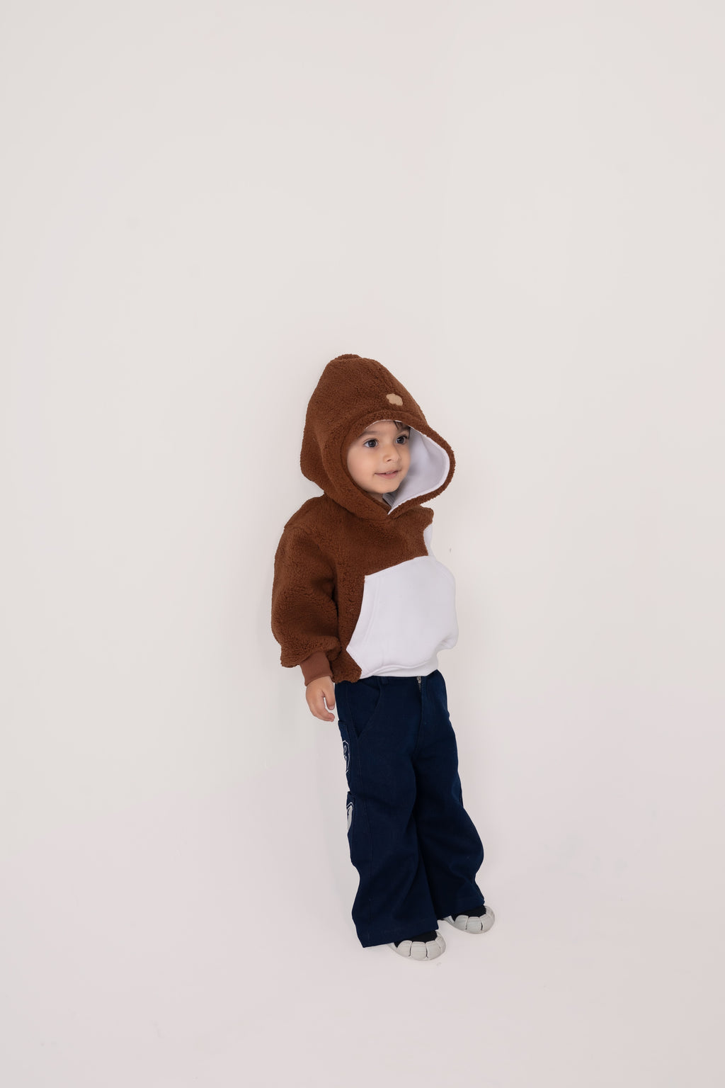 Adorable toddler wearing a plush brown and white hoodie with navy pants against a neutral background