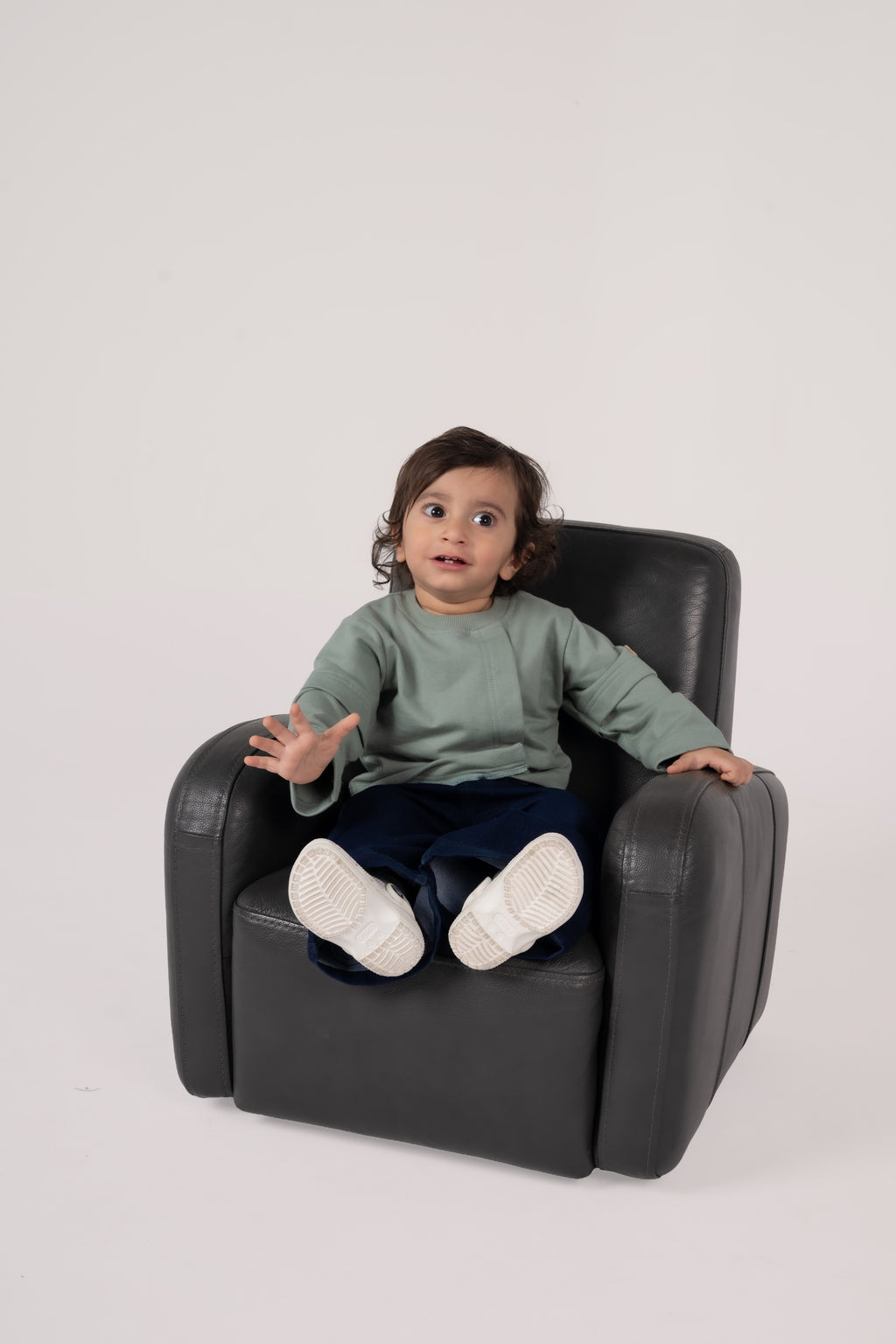 Toddler in stylish outfit sitting comfortably on a sleek black leather chair in a minimalist setting