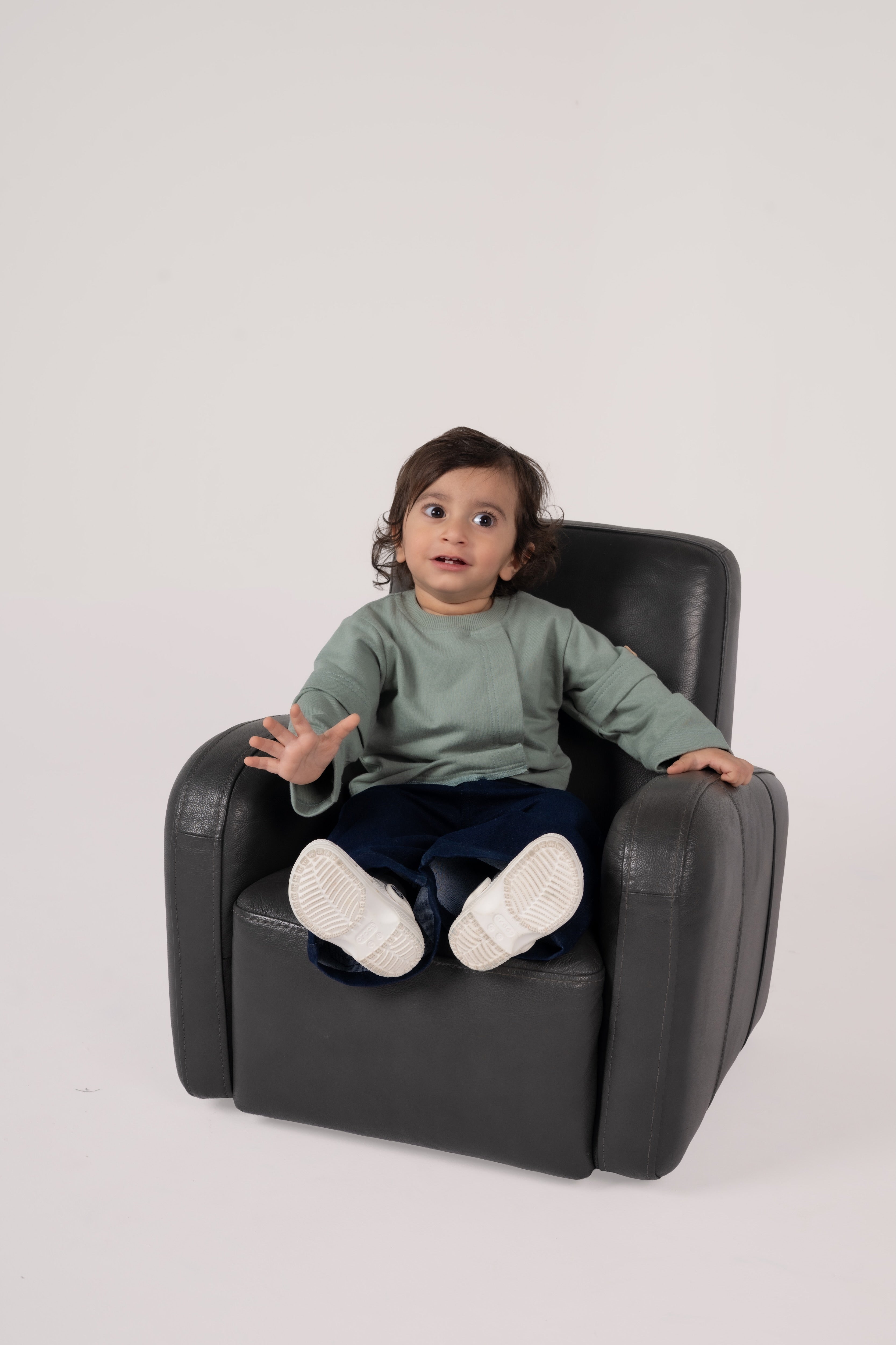 Toddler in stylish outfit sitting comfortably on a sleek black leather chair in a minimalist setting