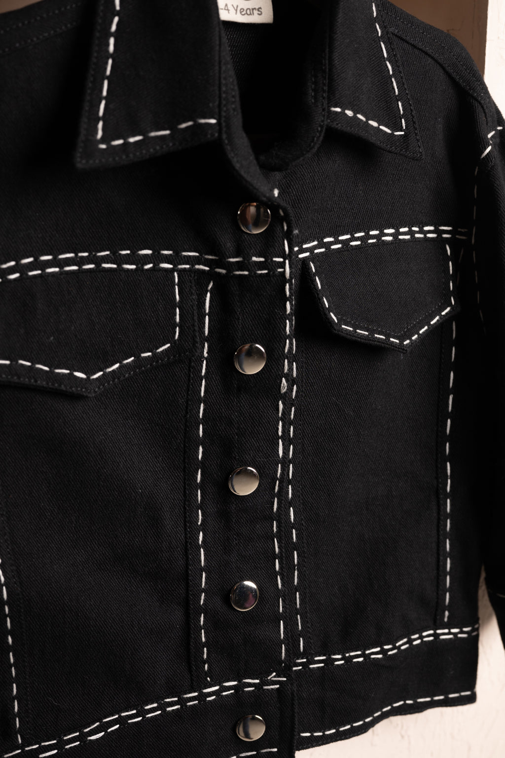 Close-up of black denim jacket with white contrast stitching and silver snap buttons