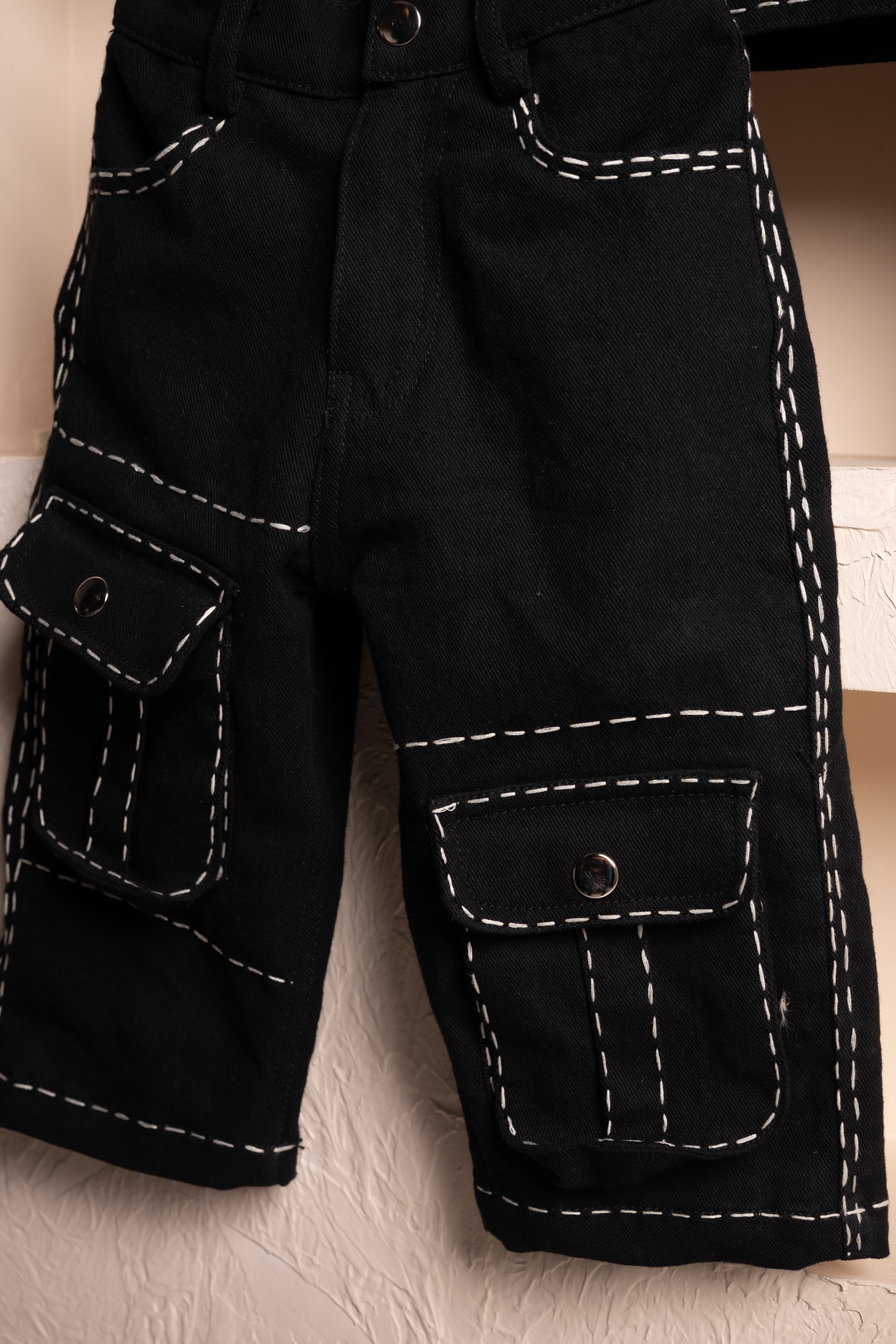 Black pants with white contrast stitching and flap pockets, showcasing refined craftsmanship
