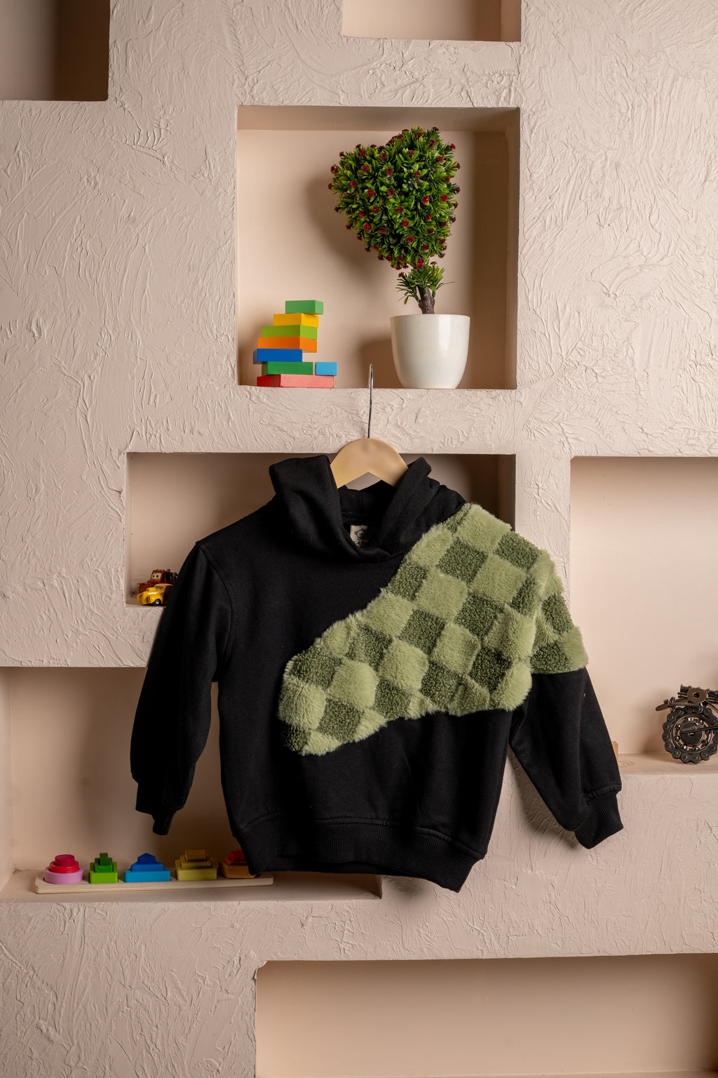 Luxurious black hoodie with green checkered plush detail displayed in beige textured wall niches with decorative items
