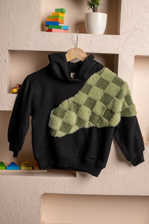 Luxurious black hoodie with green checkered plush design displayed on textured beige wall