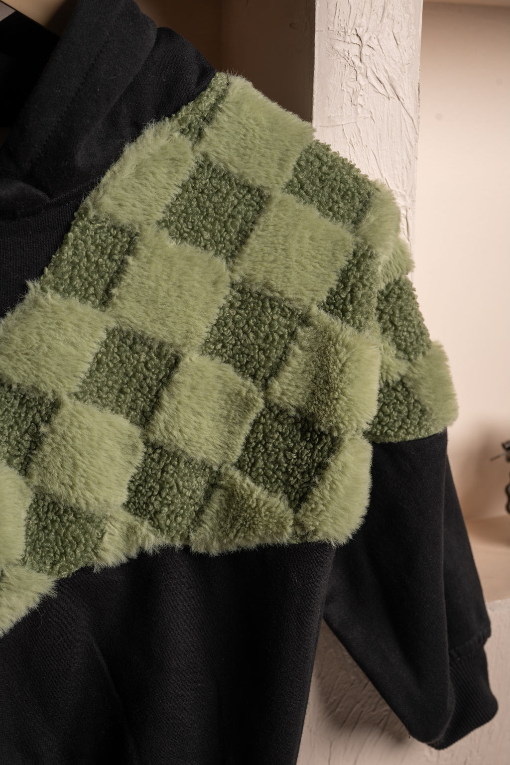 Luxurious black hoodie with green checkered faux fur shoulder detail in a cozy setting