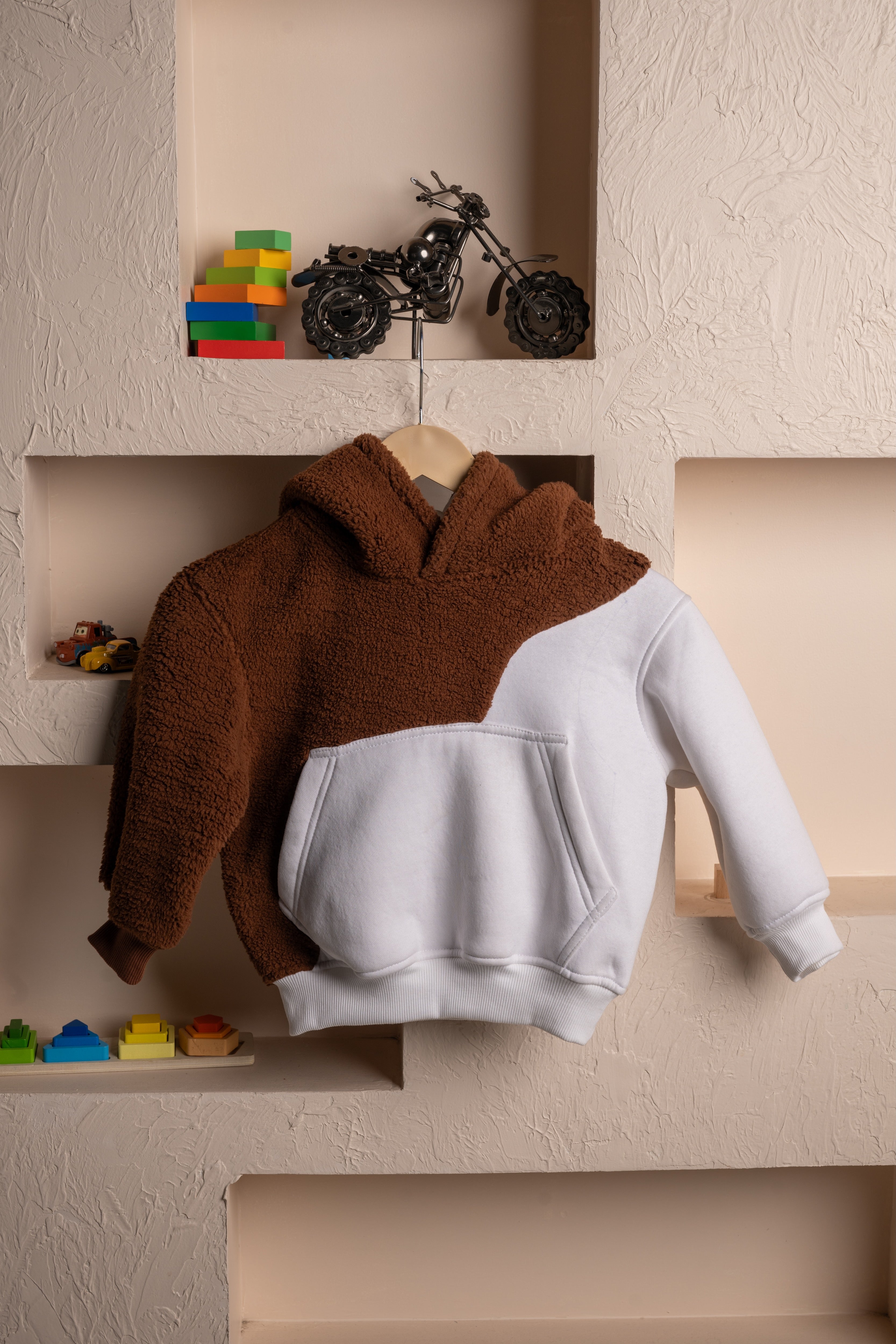 Luxurious brown and white sherpa hoodie hanging on textured beige wall with decorative shelves