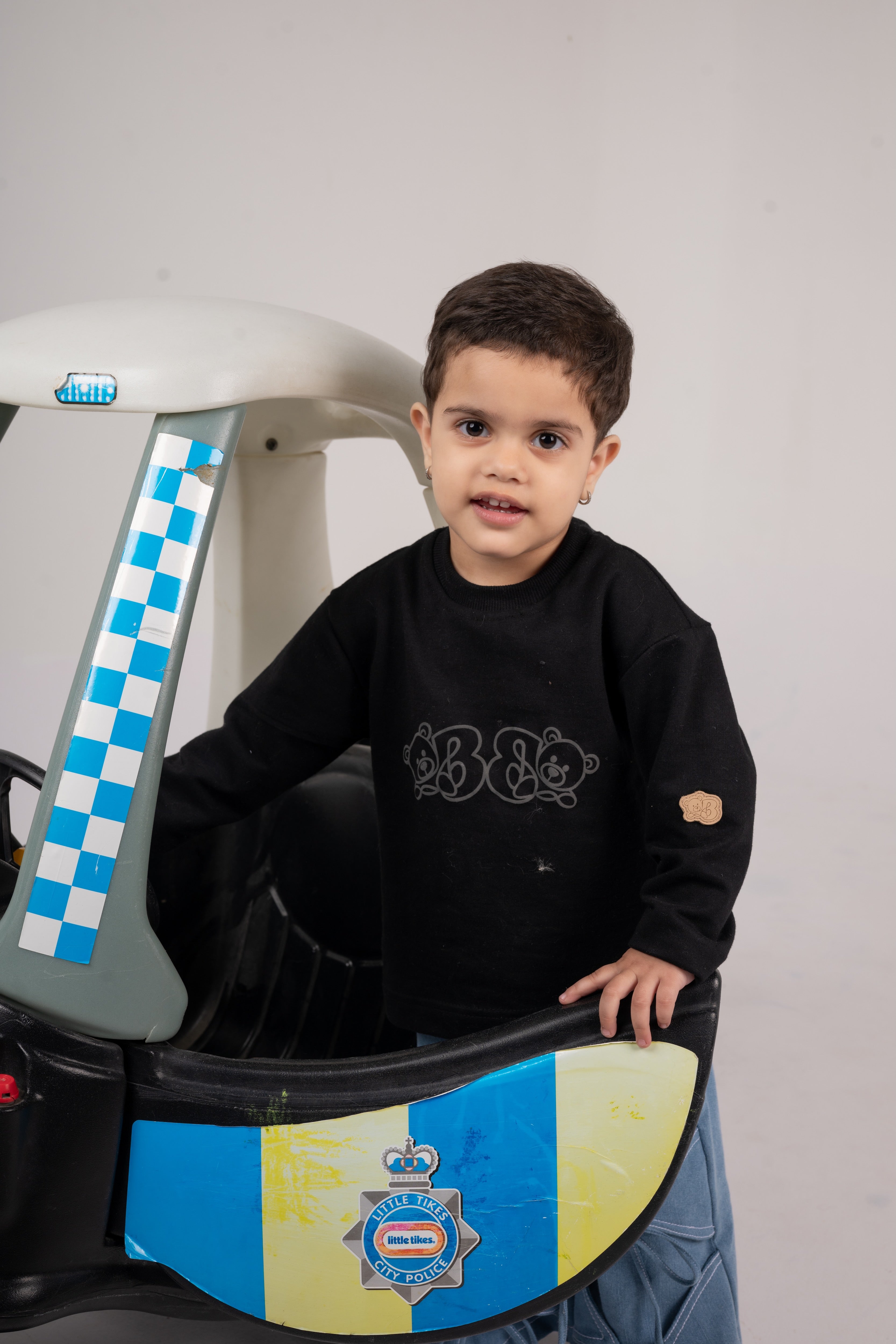 Young child in stylish black sweater posing with a colorful Little Tikes police toy car