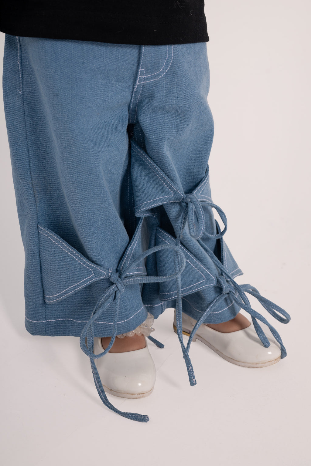 Luxury light blue denim pants with unique bow tie details paired with white patent leather shoes