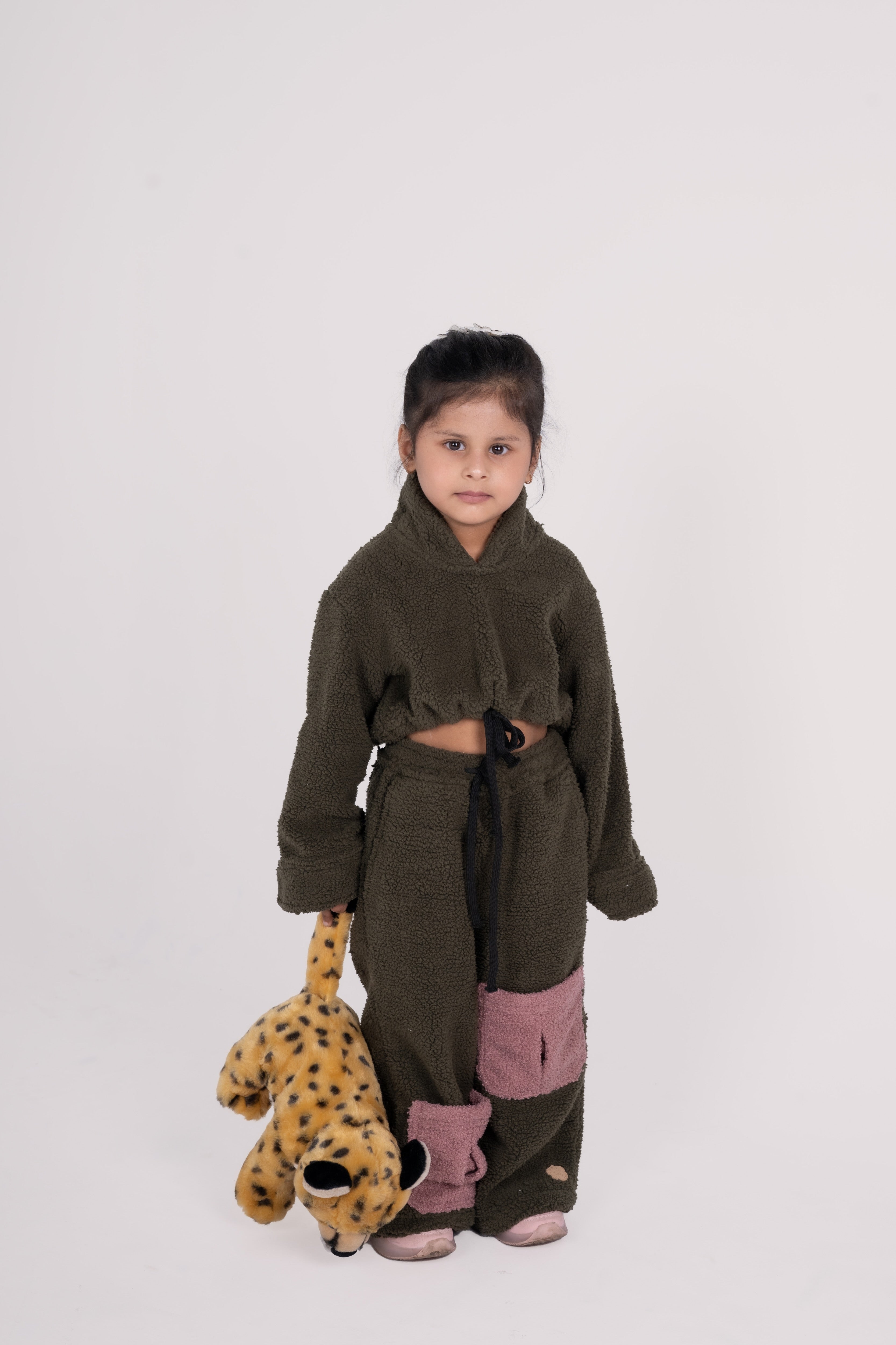 Young girl in cozy olive green fleece outfit with pink patches holding leopard plush toy