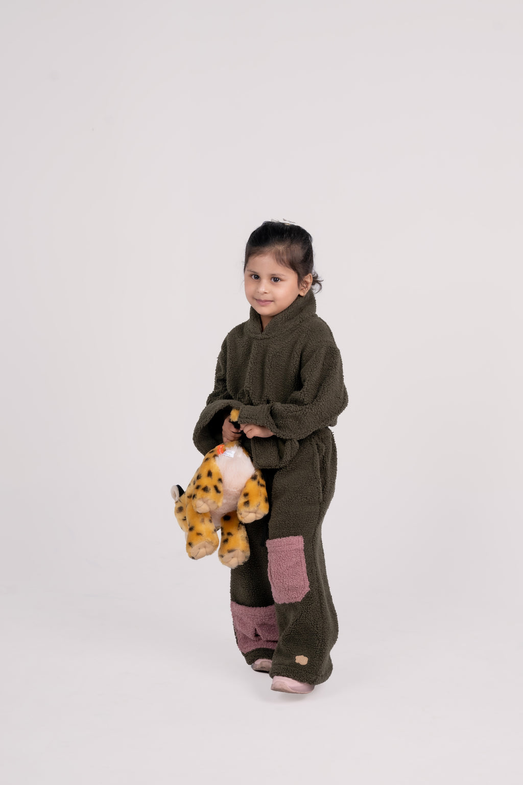 Young girl in olive green plush loungewear with pink patches holding a spotted plush toy