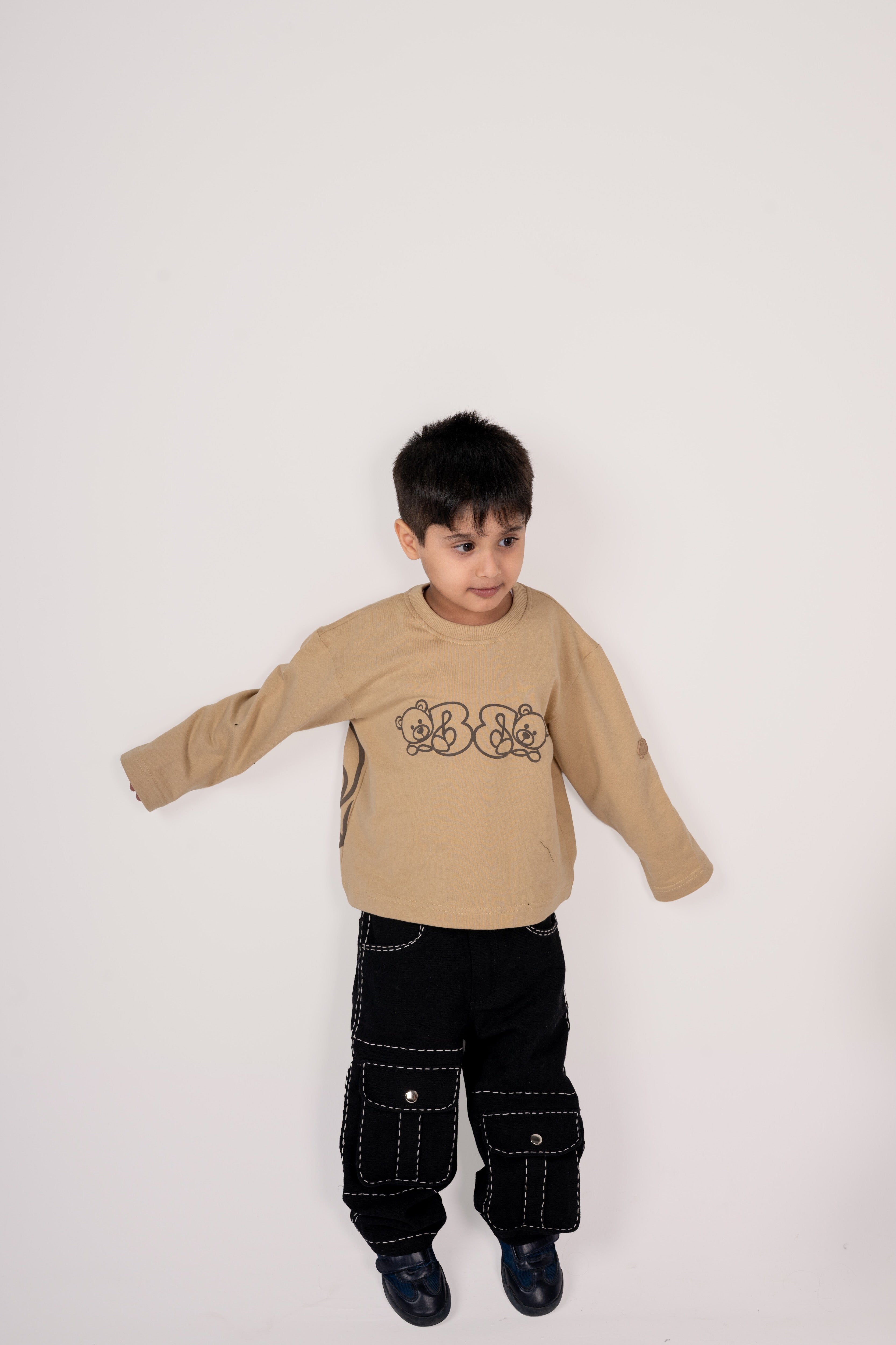 Young boy in beige designer sweatshirt with teddy bear prints and black cargo pants with white stitching