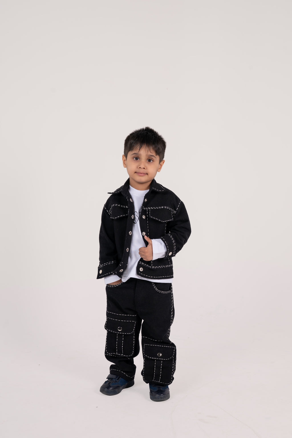 Stylish young boy in black contrasting stitch jacket and cargo pants with navy shoes on white background