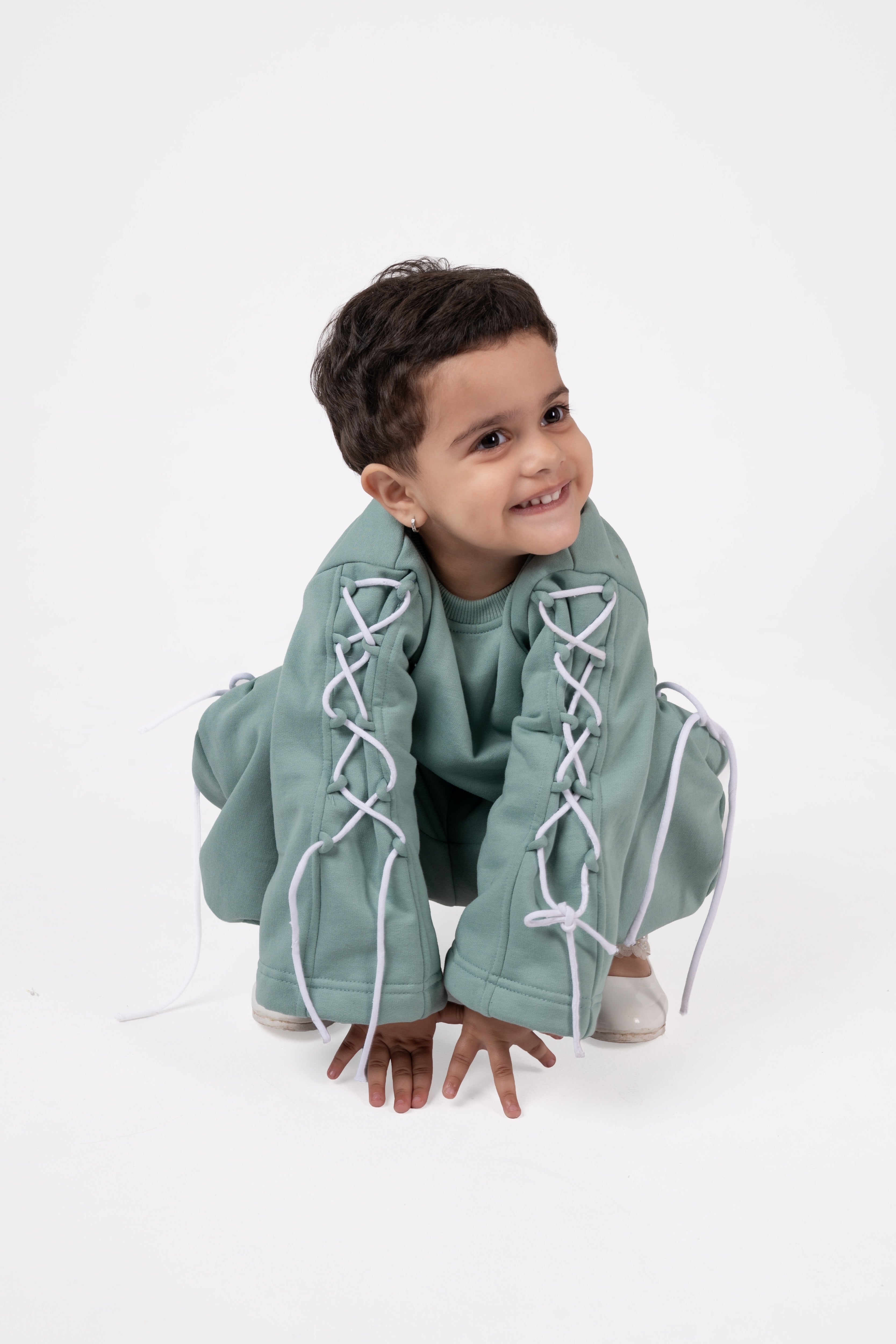Smiling child wearing sage green lace-up sleeves outfit on white background, stylish kidswear