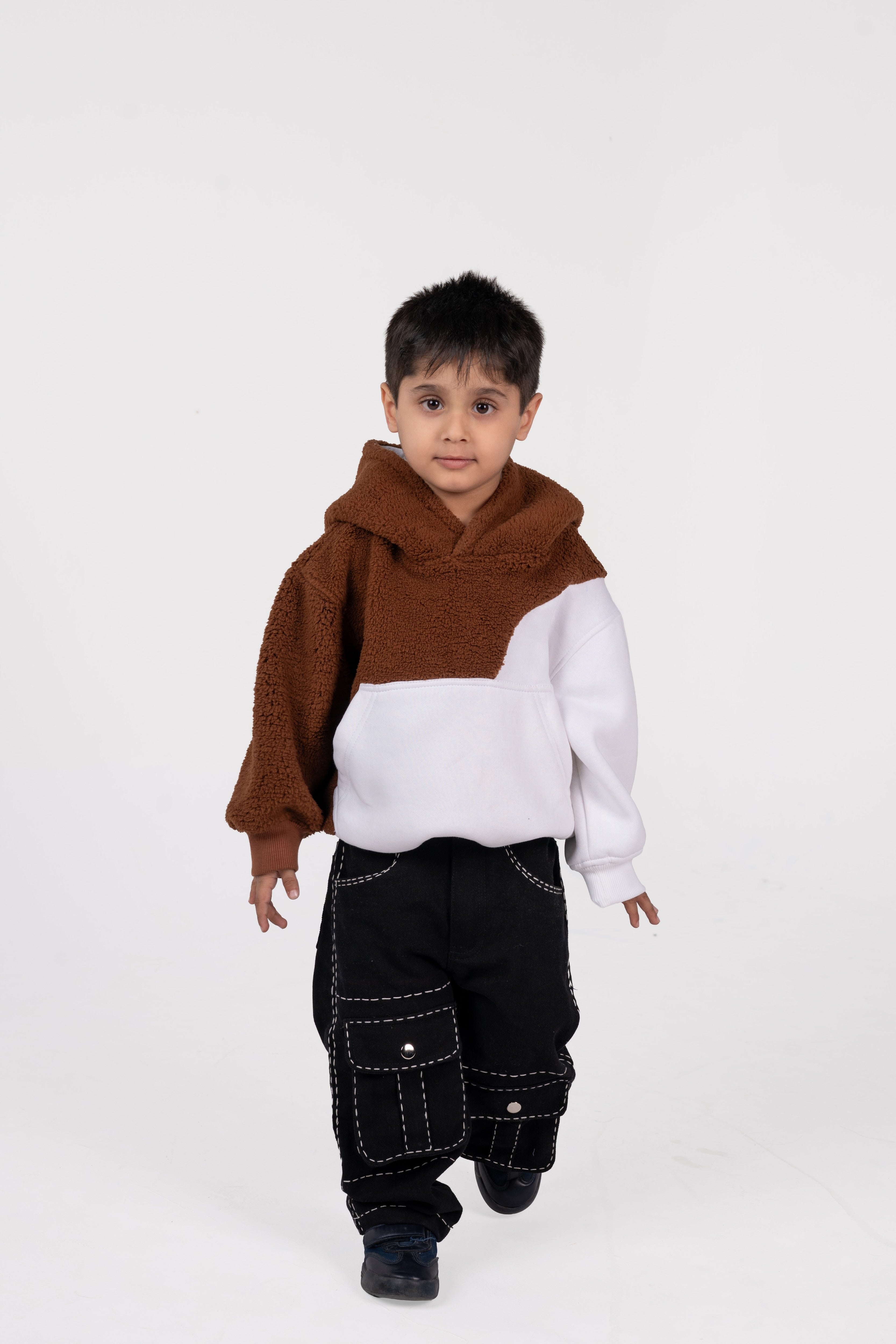 Young boy wearing a stylish brown and white fleece hoodie with black cargo pants, minimalist studio background