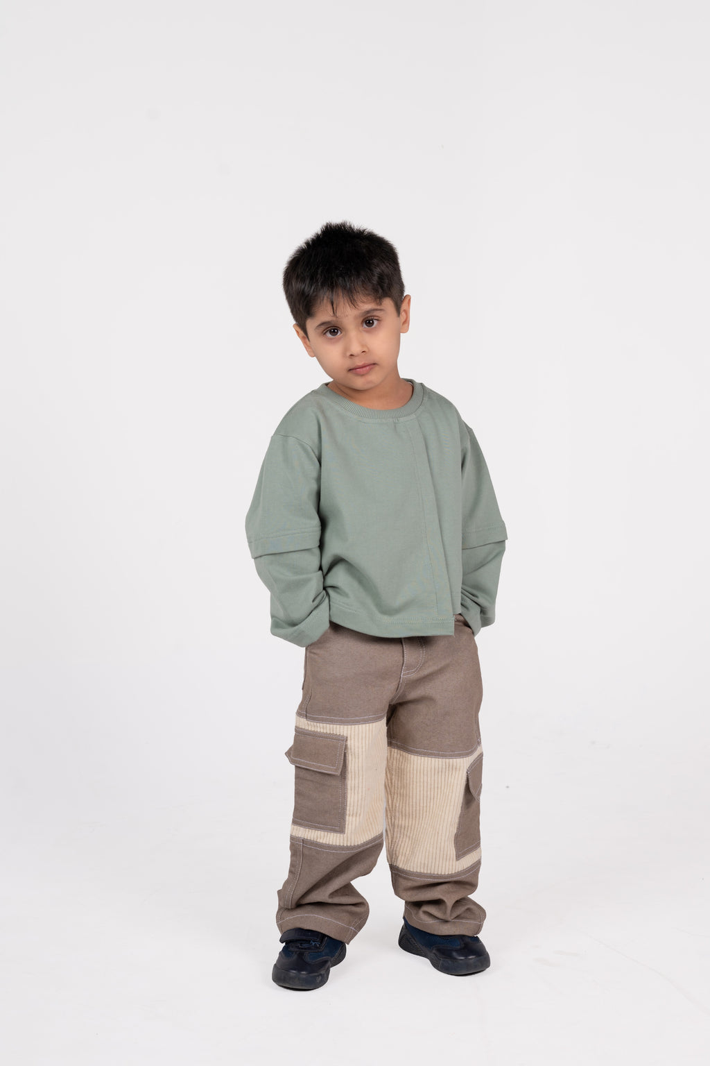 Young boy in stylish green sweatshirt and taupe cargo pants posing against white background
