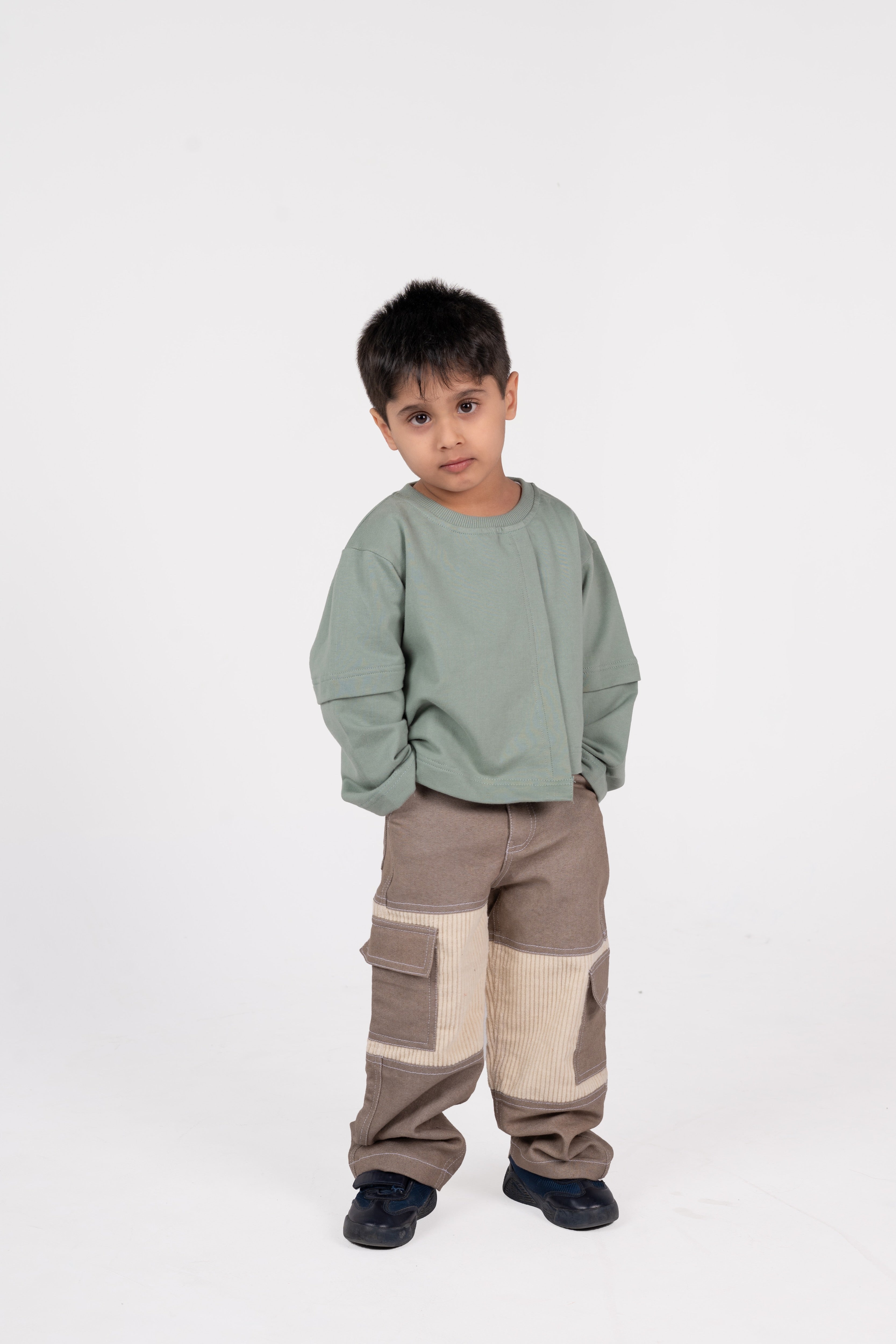 Young boy in stylish green sweatshirt and taupe cargo pants posing against white background