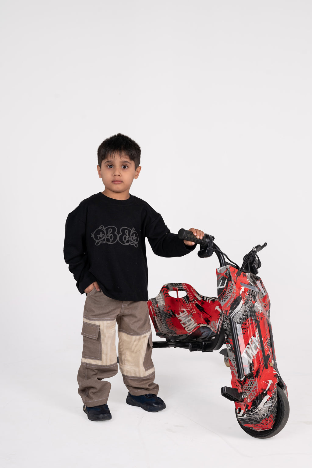 Stylish young boy in trendy patchwork pants with a red patterned electric drift trike