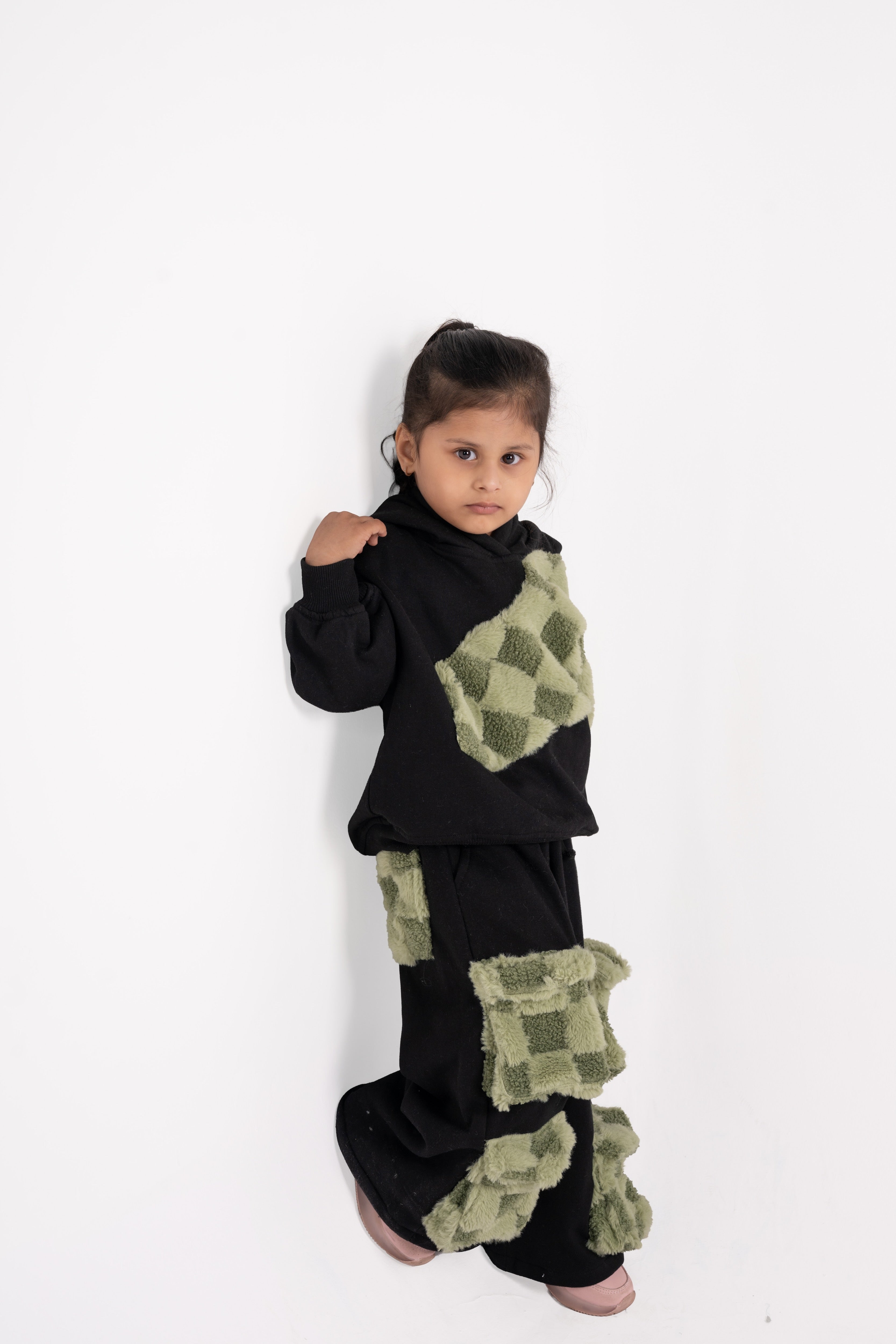 Stylish young girl in black outfit with checkered green fur patches on hoodie and pants