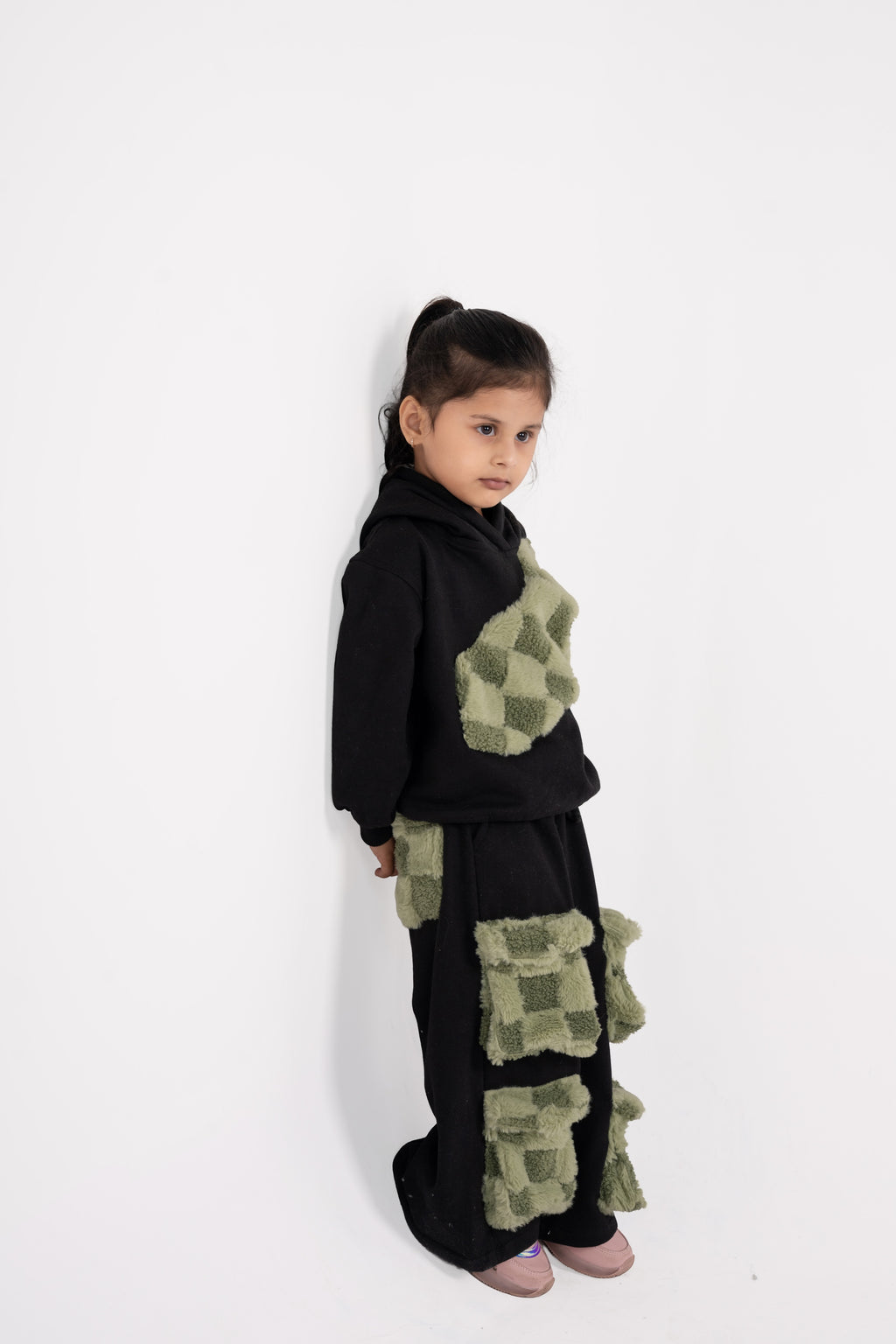 Young girl in black outfit with luxurious green plush checkered patches posing against white background