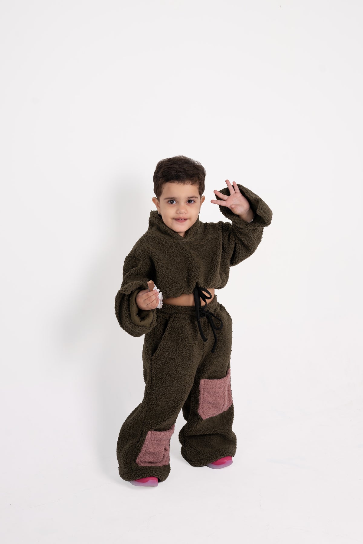 Stylish toddler in plush olive fleece outfit with pink patch pockets on white background