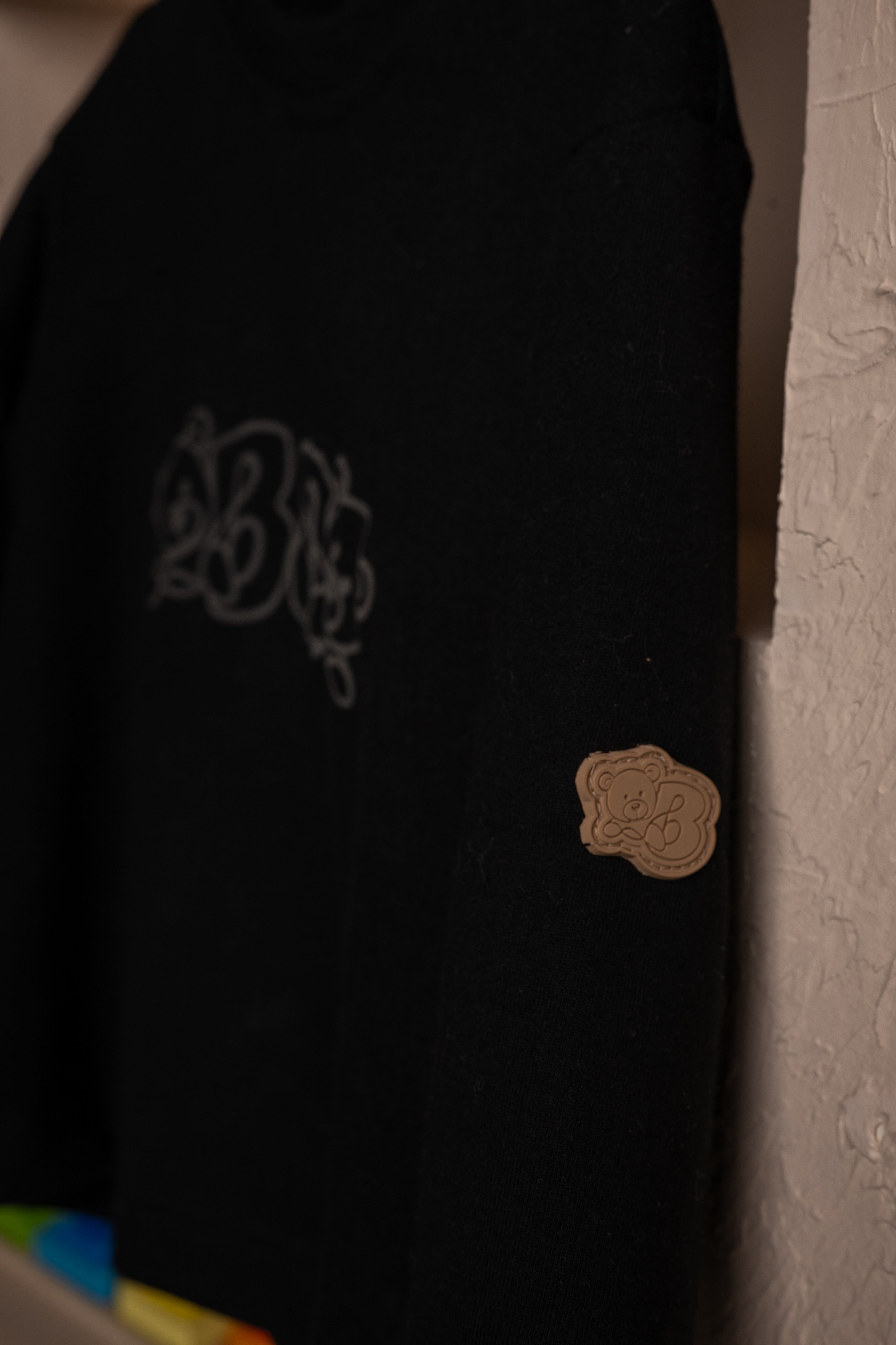 Black luxury sweater with intricate logo embroidery and a tan teddy bear patch on sleeve
