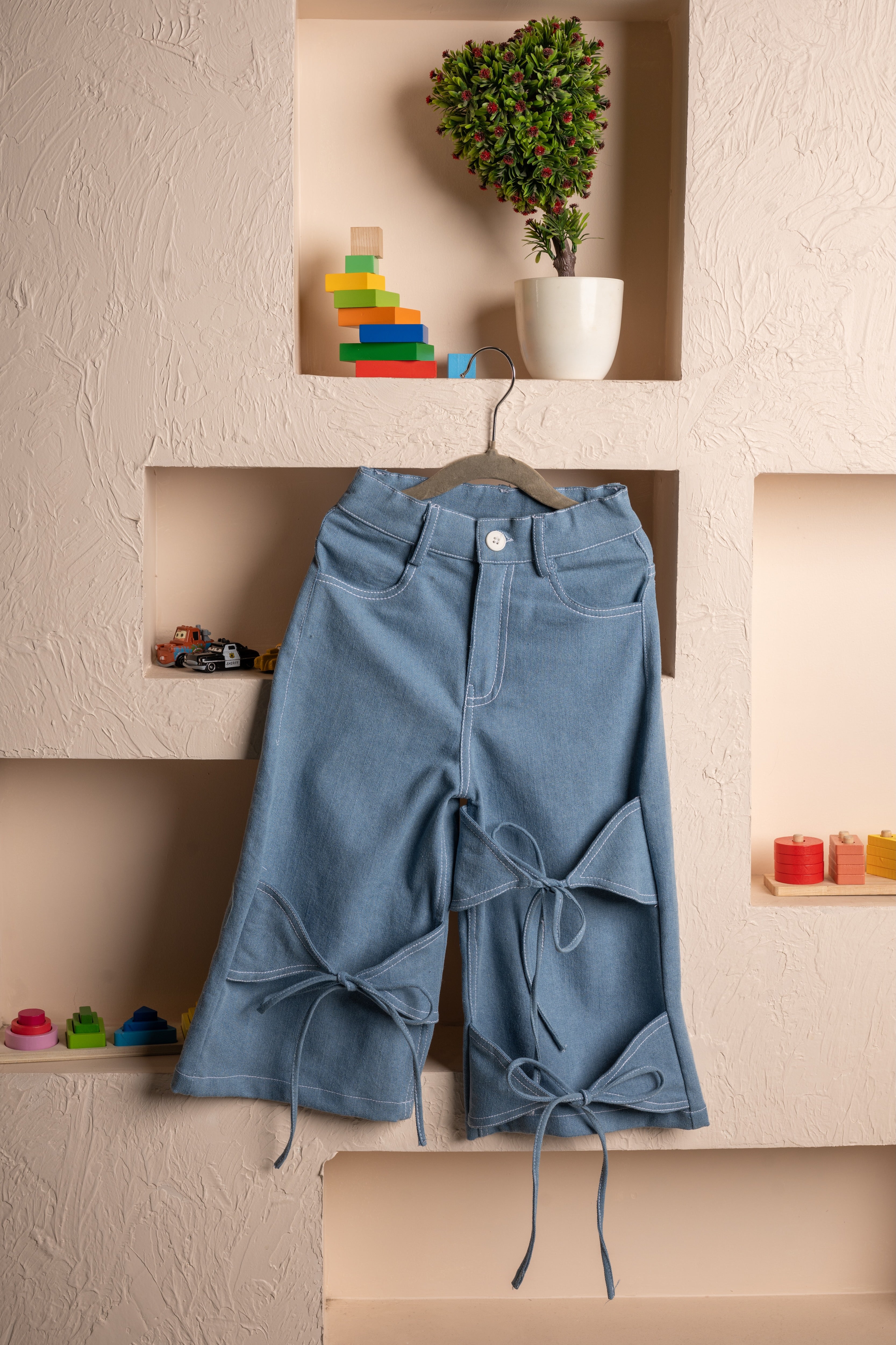 Elegant light blue cropped jeans with unique bow cut-out details displayed on textured beige wall niche
