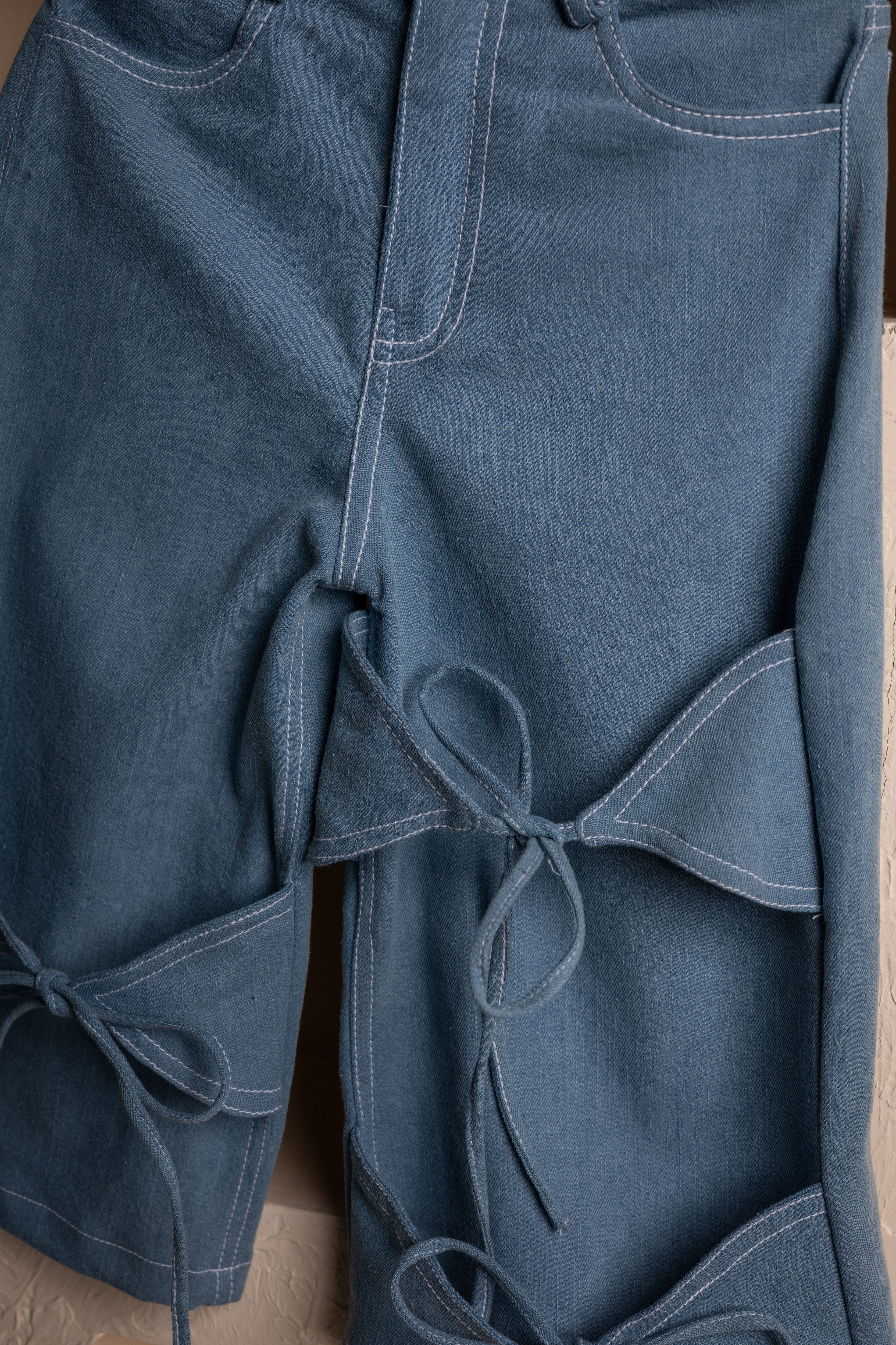 Luxury blue denim pants with elegant bow tie details and white stitching